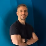 Smiling man with short hair and beard wearing a black shirt standing with arms crossed.